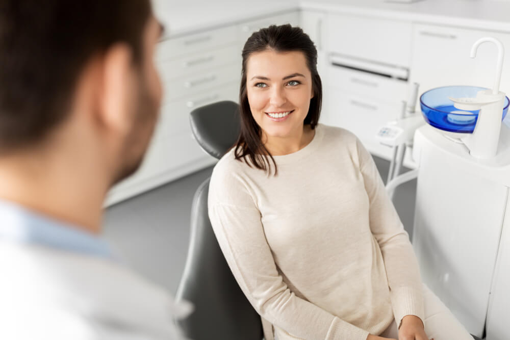 smiling female patient talking to dentist at dental clinic